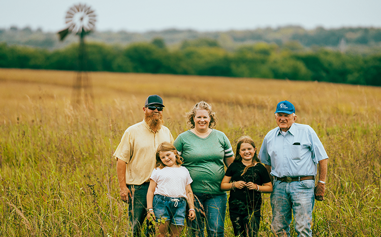 Grandfather, mom, dad and two daughters stand proudly in a field on farm
