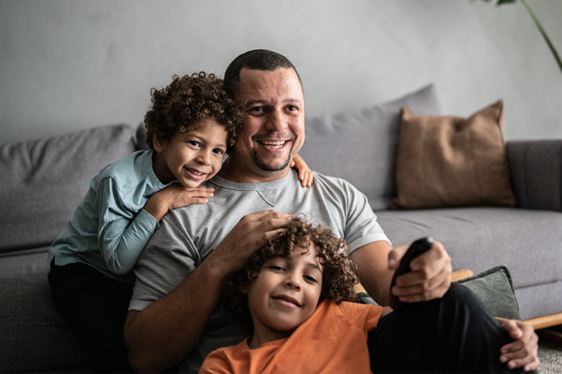 smiling parent sits on floor in front of couch with two children