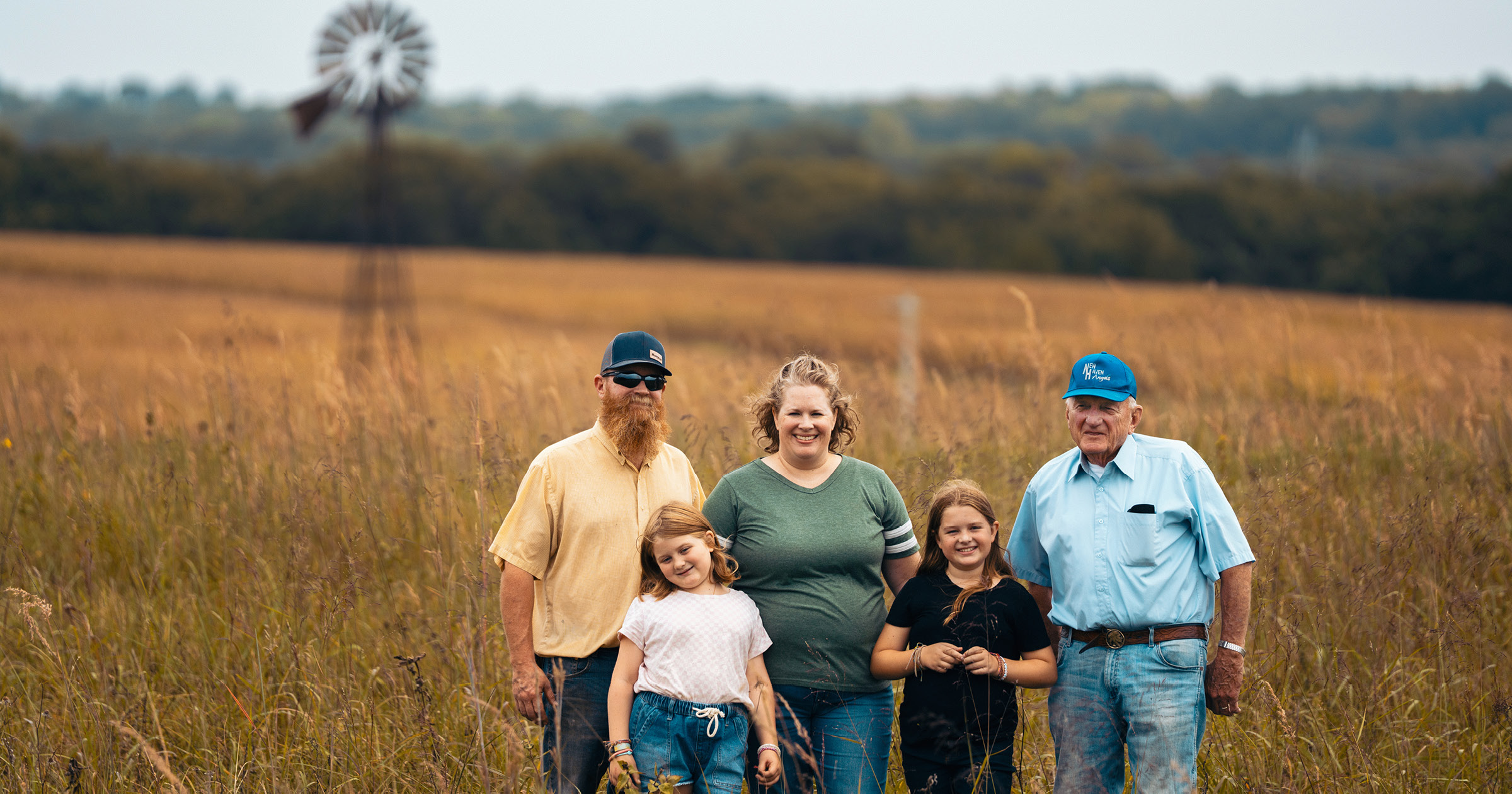 a Kansas family stands in a field with a windmill in the background
