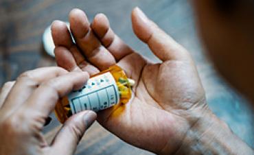 Person pours pills from a prescription bottle into an open hand.