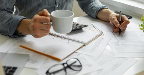 A person holds a mug in one hand and a pen in the other hand while doing paperwork.