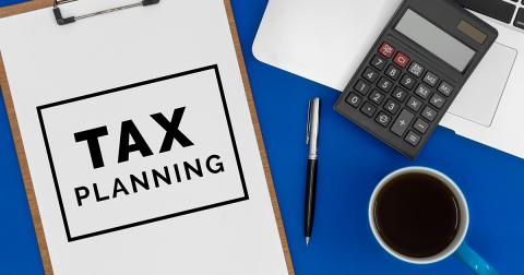 a clipboard with a paper that says TAX PLANNING, pen, calculator, and coffee mug on a desk