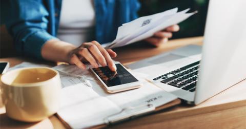 a person holding bills in one hand uses a calculator with the other hand